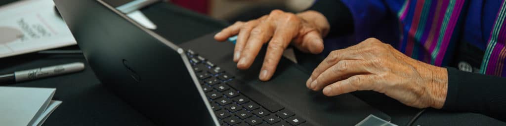 An elderly persons hands resting on a laptop keyboard.