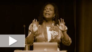 A video still image of Jacqui Lewis during the Universal Christ conference with a play button overlay.