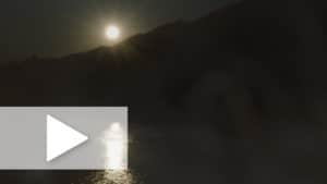 A night time image with a foggy moon over a dark hill with a play button overlay.