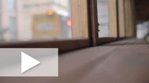 A photograph of a window sill looking out towards a blurry city bus with a play button overlay.