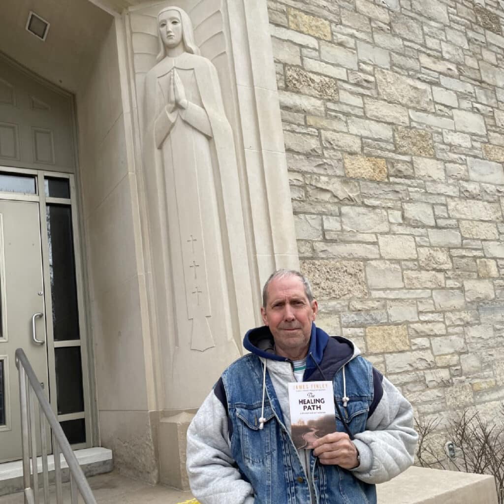 Denny D. standing in front of a church holding the book.