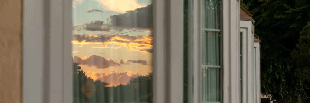 A row of windows at dusk are dark except one that is lit up by the reflection of a multi-colored sunset