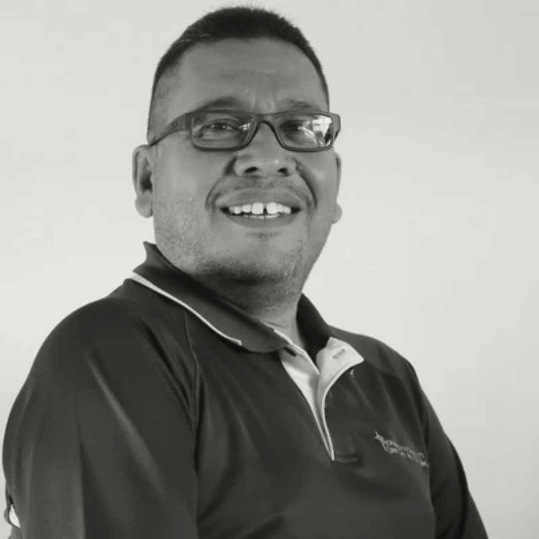 Black and white portrait of a middle-aged man with glasses smiling confidently. He is wearing a polo shirt against a plain background.