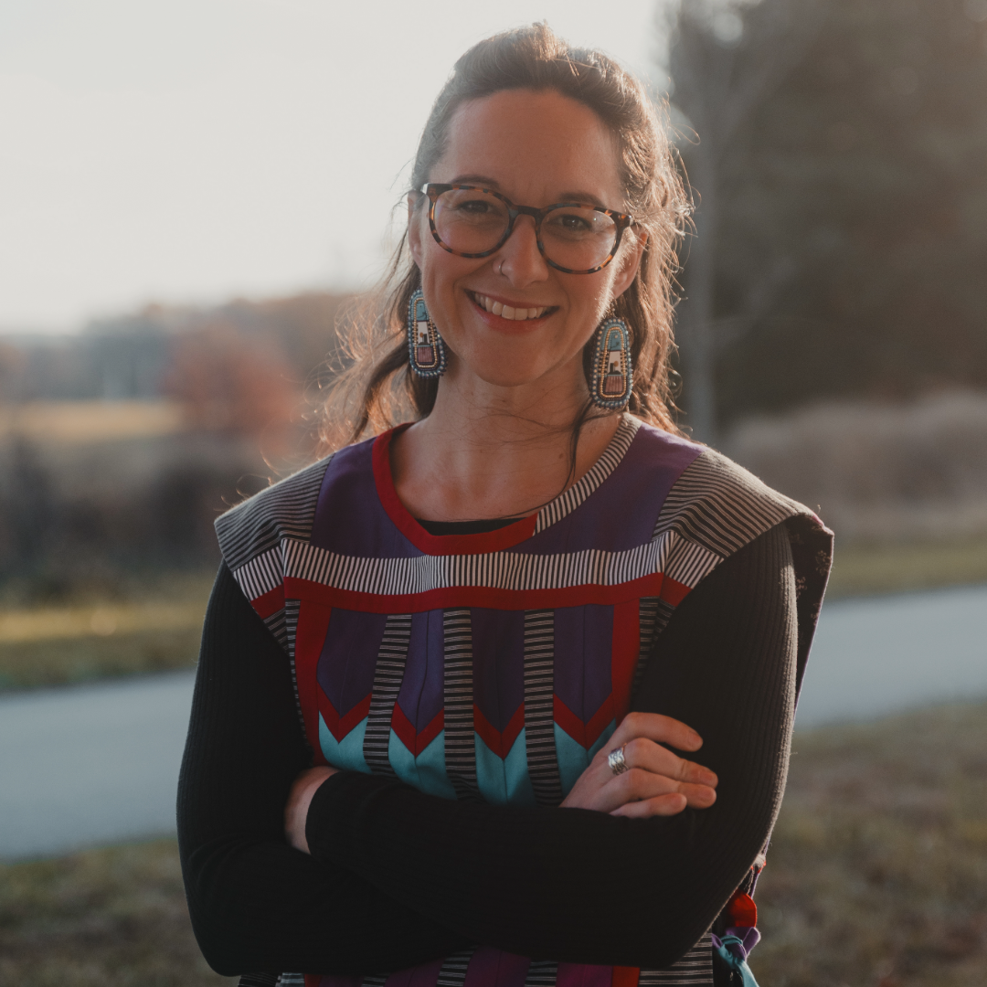 A portrait of Kaitlin Curtice wearing a vibrant, patterned top and a distinctive medallion necklace, exuding confidence.