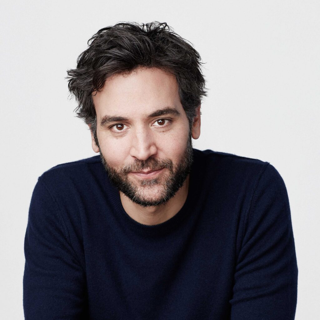 Josh Radnor smiling and wearing a navy blue sweater.